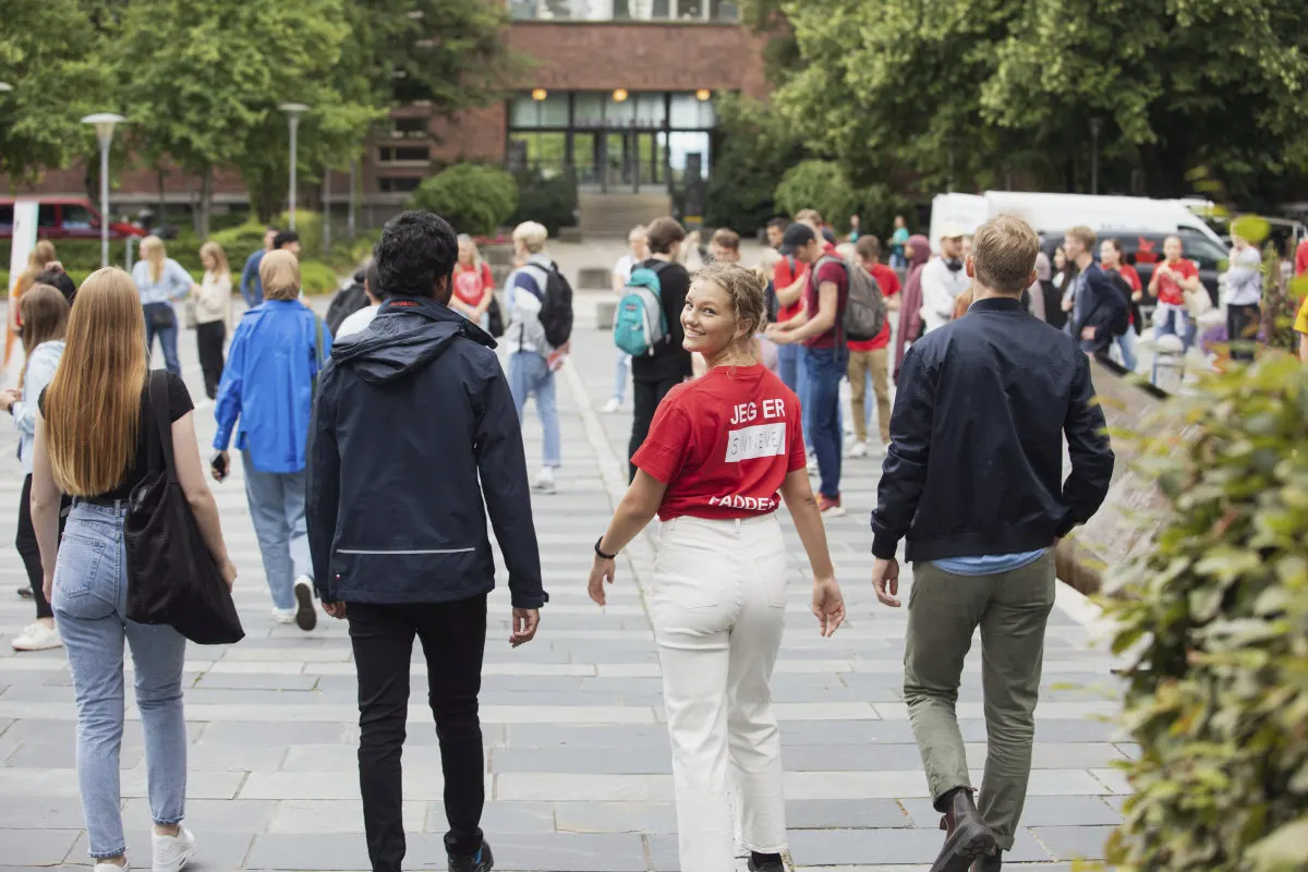 UiO studenter g?r side om side fra fotografen. I midten en fadder i UiO t-skjorte som snur seg og smiler til kamera.